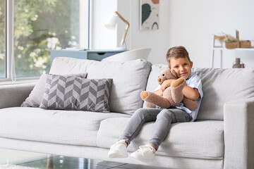 Obraz premium Cute little boy hugging teddy bear on sofa in living room
