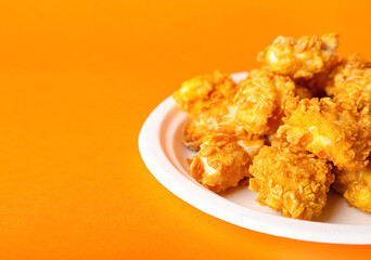 Plate with tasty fried popcorn chicken on orange background, closeup
