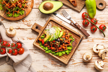 Composition with tasty Belgian waffles and vegetables on light wooden background