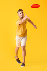 Fototapeta na wymiar Handsome young man catching frisbee on yellow background