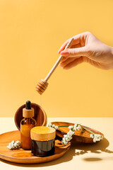 Woman pouring honey onto jar of cosmetic products, closeup