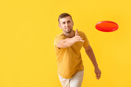 Handsome young man throwing frisbee on yellow background
