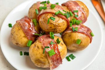 Plate of tasty baked potatoes with bacon on light background, closeup