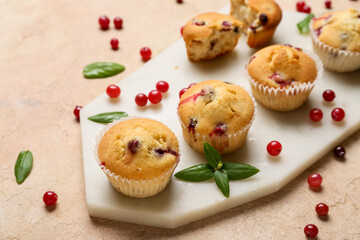 Board with delicious cranberry muffins on beige background