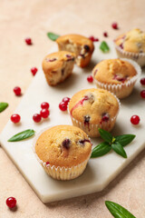 Board with delicious cranberry muffins on beige background