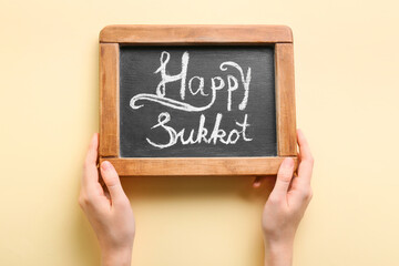 Hands holding chalkboard with text HAPPY SUKKOT on color background