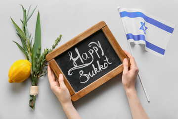 Hands with chalkboard, flag of Israel and Sukkot festival symbols on light background