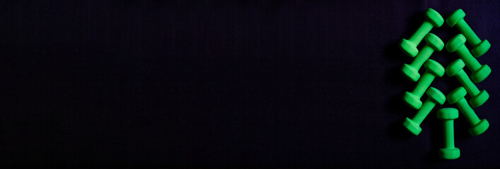 Gym Fitness minimalistic banner with creative Christmas Tree made of green dumbbells on black yoga mat. Flat lay, top view, copy space