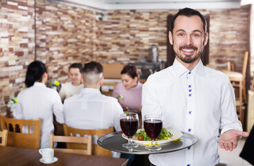 Fototapeta na wymiar Cheerful male waiter serving rural restaurant guests at the table