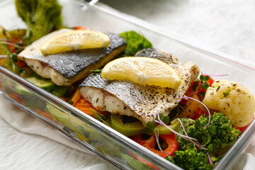 Baking dish of tasty sea bass fish with vegetables on light background