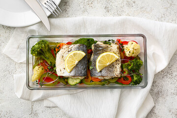 Baking dish of tasty sea bass fish with vegetables on light background