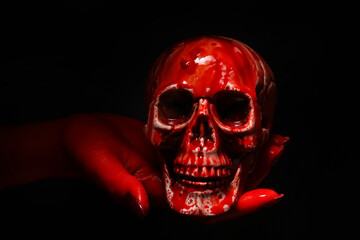 Hand with bloodstained human skull on black background