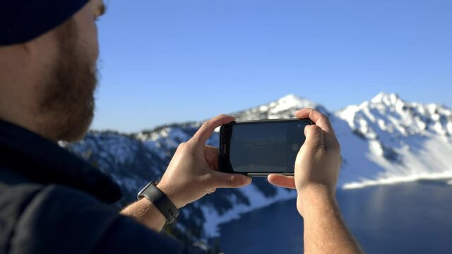 Man taking a photo of beautiful snowy mountain range and lake