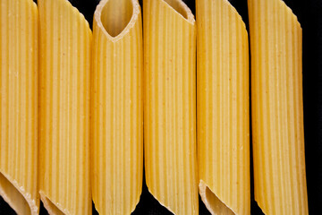 Raw penne rigate pasta close up on black background.