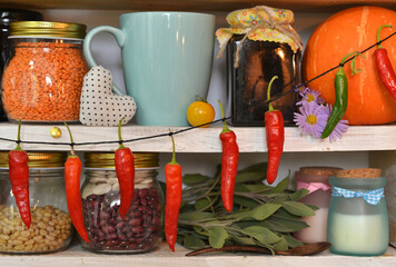 Old cup, glass jars and bottles with jam, spice and beans, pumpkin and herbs on wooden counter in the vintage kitchen.
