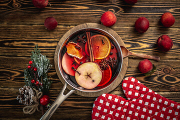 Pot with fragrant spicy hot mulled wine on a wooden table surrounded by festive accessories and fruits. Concept of a cozy holiday atmosphere, New Year and Christmas mood. Top view