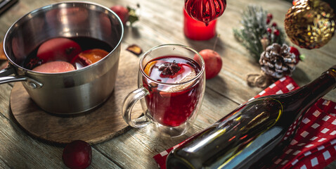 Spicy aromatic hot mulled wine in a saucepan and a clear glass on a wooden table with festive accessories. Concept of a cozy holiday atmosphere, New Year and Christmas mood