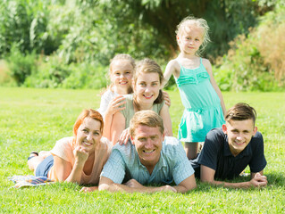 Fototapeta premium Portrait of big family with parents and four children lying together on green lawn outdoors