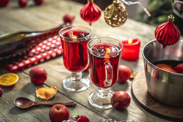 Spicy aromatic hot mulled wine in a saucepan and a clear glass on a wooden table with festive accessories. Concept of a cozy holiday atmosphere, New Year and Christmas mood
