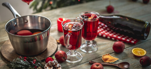 Spicy aromatic hot mulled wine in a saucepan and a clear glass on a wooden table with festive...