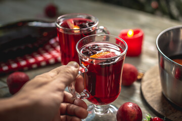 Hand is holding a glass with fragrant spicy mulled wine decorated with fruits and spices. Concept of a cozy festive atmosphere, New Year and Christmas mood
