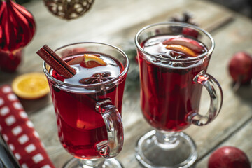 Spicy aromatic hot mulled wine in a couple clear glasses on a wooden table with festive accessories. Concept of a cozy holiday atmosphere, New Year and Christmas mood