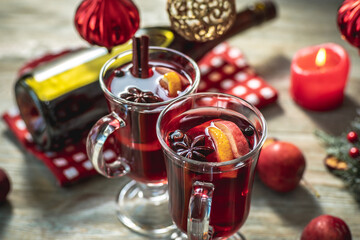 Spicy aromatic hot mulled wine in a couple clear glasses on a wooden table with festive accessories. Concept of a cozy holiday atmosphere, New Year and Christmas mood