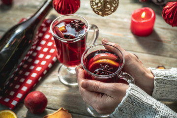 Woman in a sweater is holding a clear mug with fragrant spicy mulled wine decorated with fruits and...