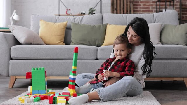 Care and child development, leisure concept. Happy caucasian Mother and her son look at the camera and smiling. Family spending free time at home. Childhood, playthings and house concept.