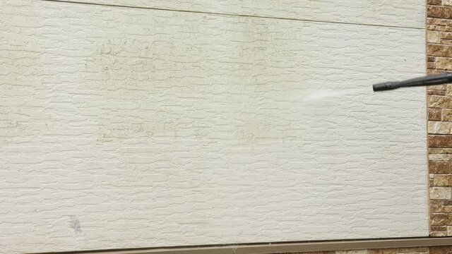 Man cleaning walls with high pressure power washer. Washing cladding walls house.