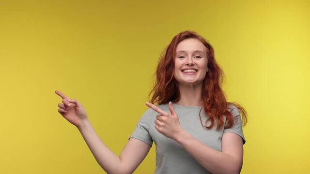 Excited surprised ginger young woman 20s in casual t-shirt posing isolated on yellow color background in studio. Girl Pointing index fingers aside say wow doing winner gesture People lifestyle concept