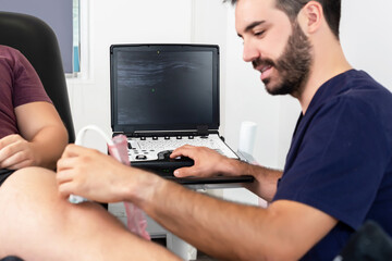 Physiotherapist performing an ultrasound of the knee on a patient lying on the stretcher. Selective...