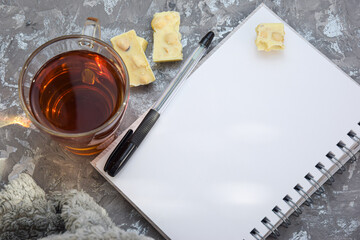 Composition of a cup of tea, a notebook and a pen on a gray background. A soft blanket with a cup of hot tea and an open book with a pen on a rough blackboard background with a place to copy