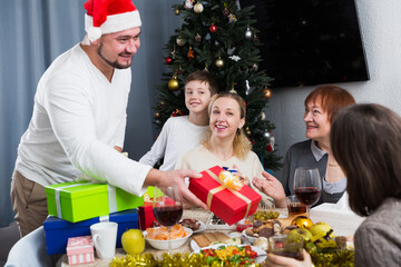 Smiling man giving presents to his family during Christmas celebration at home