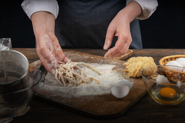 Women's hands, flour and dough. A woman in an apron cooking dough for homemade baking, a rustic home cozy atmosphere, a dark background with unusual lighting.