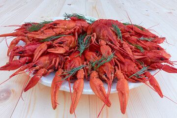 On a wooden table, a portion of boiled crayfish sprinkled with dill in a plate.
