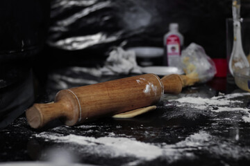 Closeup of a wooden rolling pin on top of the dough with flour in the foreground