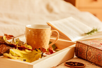 Hot tea or coffee in a ceramic mug , autumn leaves on wooden tray, open book on the bed. Cozy weekend at home