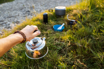 Kettle of silver color to hold in your hand against the background of nature. Tourist breakfast. Cooking in camping conditions.