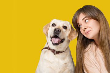 Portrait of a young beautiful girl with long hair and a labrador dog, on a yellow background. The image has a blank space for your text.