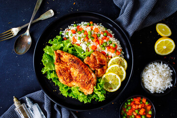 Fried chicken breast with white rice, green peas and carrots on black wooden table