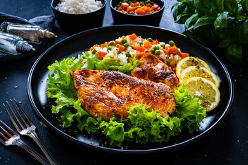 Fried chicken breast with white rice, green peas and carrots on black wooden table
