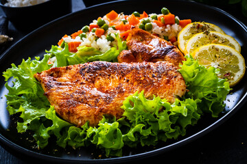 Fried chicken breast with white rice, green peas and carrots on black wooden table