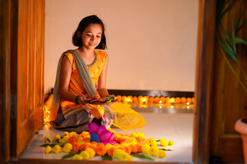 Cute indian little girl making decoration with flower and oil lamp for diwali festival at home