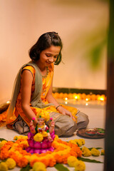 Cute indian little girl making decoration with flower and oil lamp for diwali festival at home