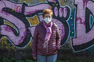 senior woman in jacket and medical mask on public wall with graffiti not subject to copyright
