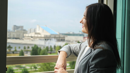 young woman in a business suit stands by an open window and looks into the distance. © lenblr