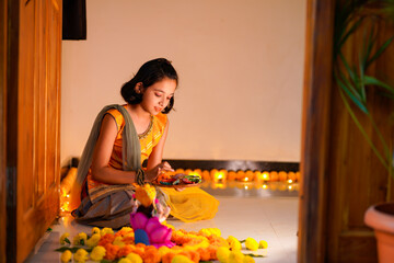 Cute indian little girl making decoration with flower and oil lamp for diwali festival at home.