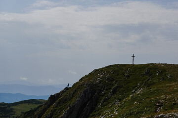 Fototapeta na wymiar summit cross on a mountain and a standing hiker in austria