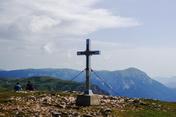 summit cross with two sitting hikers in the summer